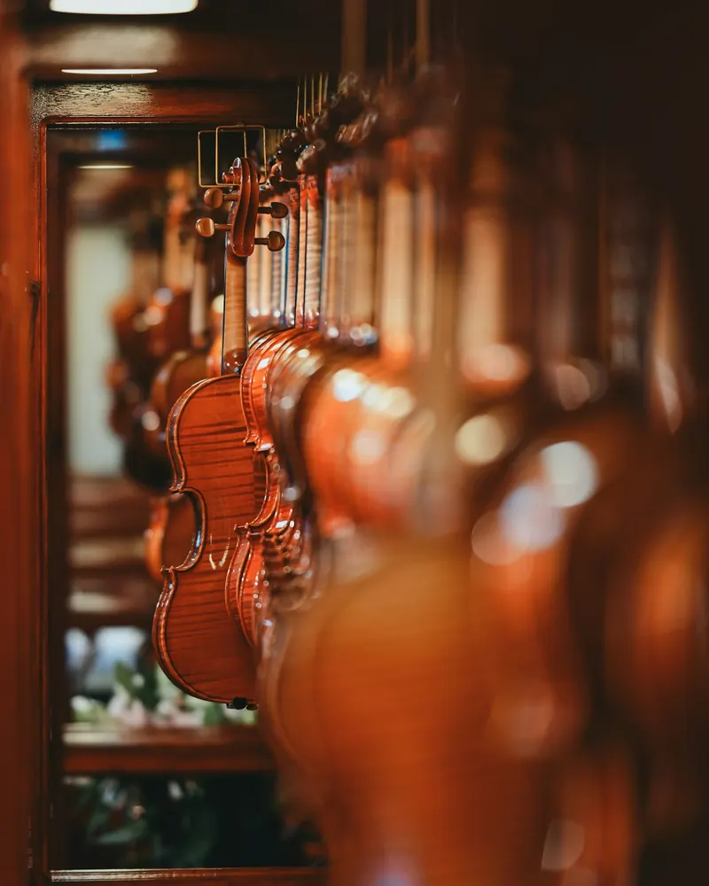 Fila de violinos envernizados pendurados pela voluta numa parede de madeira, com a madeira flamejada do fundo visível no primeiro instrumento